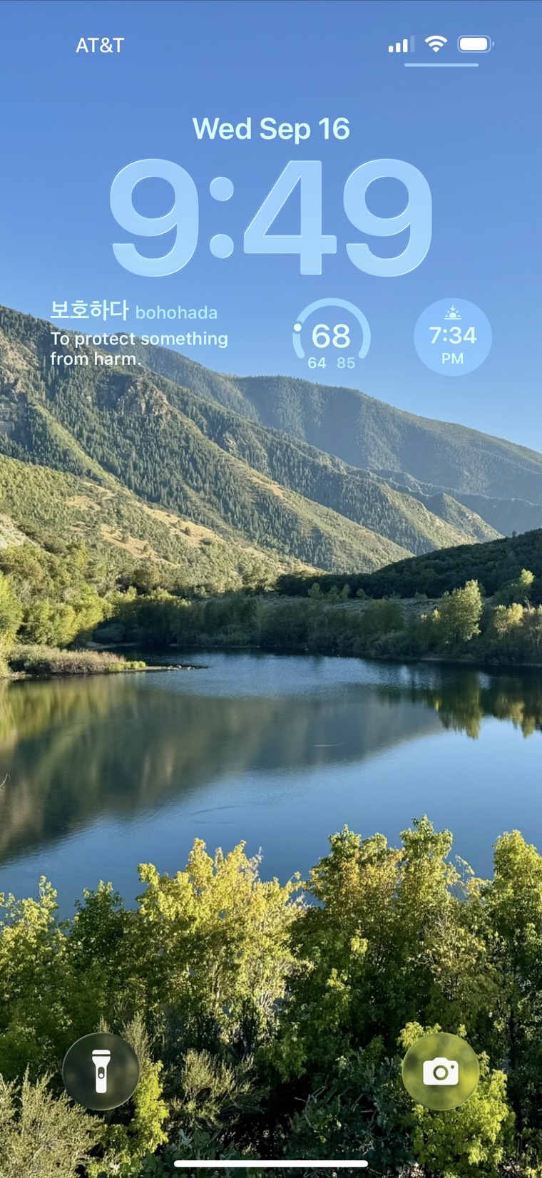 An iPhone lock screen over a mountain lake, with the Onymera widget showing the Korean word 보호하다, bohohada — to protect something from harm.